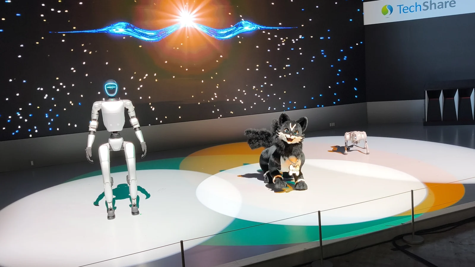 Роботы Unitree G1 слева, Visionoid FOX в центре и Unitree Go2 справа на сцене Japan Mobility Show.