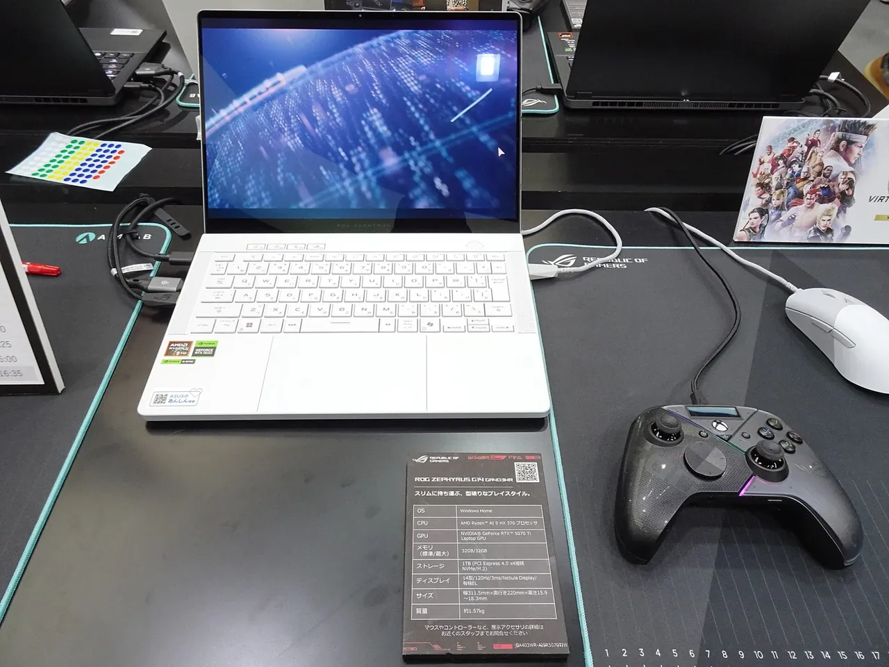 Ноутбук ASUS ROG Zephyrus G14 на выставочном столе рядом с мышью и игровым контроллером.